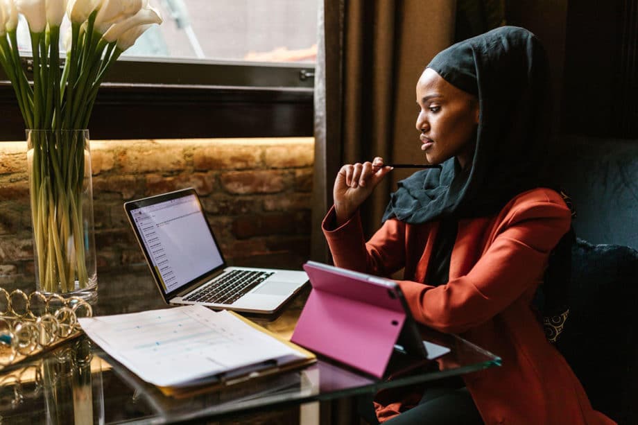 A woman wearing a hijab sitting at a table with a laptop.