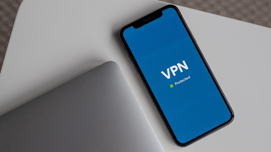 A smartphone with a VPN app displaying "Protected" lies next to an angled laptop on a white table.